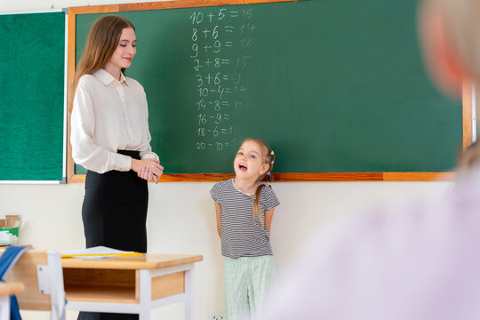 Cute girl student talking to teacher during lesson in elementary classroom, Young schoolgirl answering question in math class with teacher in classroom