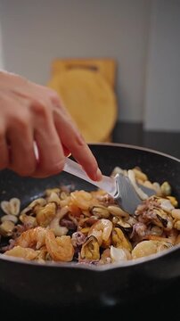Vertical video. Hand Stirs Shrimp Mussels and Squid in a Skillet, Close View of Home Seafood Preparation and Fresh Cooking Slow motion