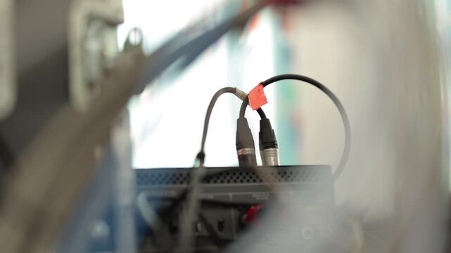 Audio cables with XLR and RCA connectors are plugged into the rear panel of a sound mixer console next to a flight case in a studio setup.