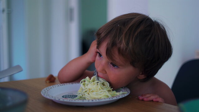 Child twirling spaghetti with fork at the kitchen table at home, focused self-feeding practice representing motor development, confidence and healthy independence