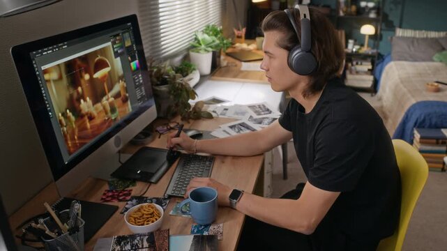 Young Asian man wearing headphones editing digital illustration on computer using graphics tablet. Footage is perfect for remote work and creative freelancing themes