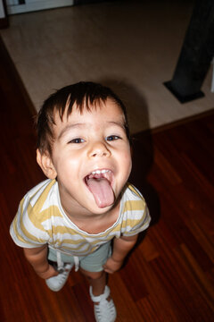 A young white boy playfully sticks out his tongue indoors on wood
