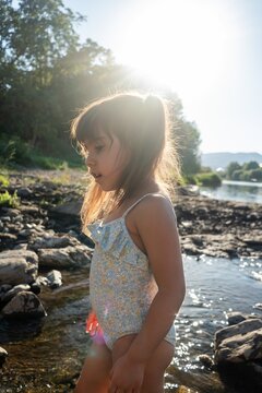 A white girl in a swimsuit explores rocky riverbank water on a sunny