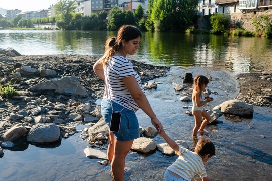 A white woman helps her son play by the riverbank with another child