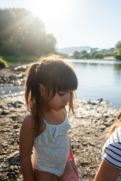 A young white girl stands by the riverbank enjoying a sunny summer day