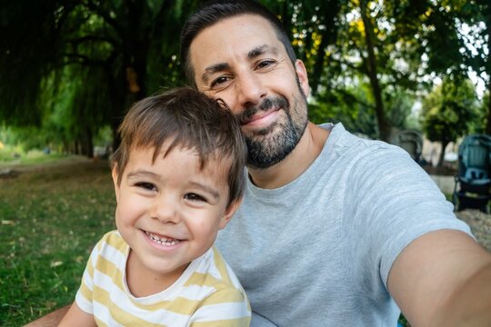 Father and son happily take a selfie together outdoors in a park