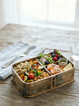 Wooden bento box filled with salmon, quinoa, roasted vegetables, and berries on a table