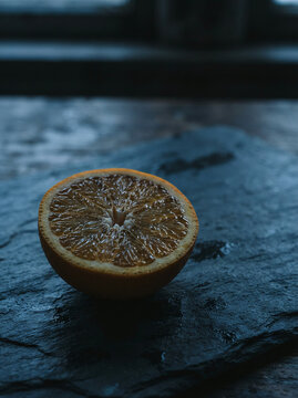 Fresh orange half with visible segments resting on a wet dark slate surface