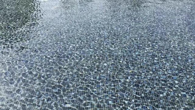 Clear shimmering water gently rippling over dark blue mosaic tile bottom of outdoor fountain with sparkling sunlight reflections