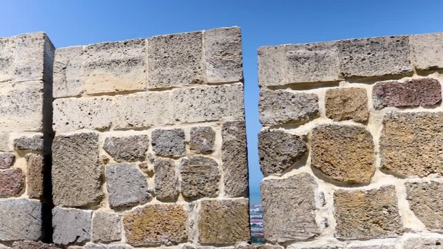 A stone wall with two windows and a blue sky in the background