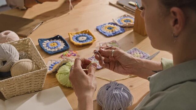 Young woman crocheting colorful yarn squares at wooden table during creative workshop. Clip is perfect for DIY craft tutorials and handmade business promotions