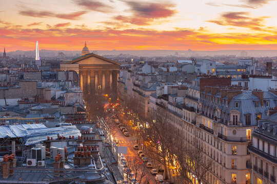 Elevated view over central Paris, France, with dense historic buildings, rooftops and illuminated streets beneath a vivid evening sky.