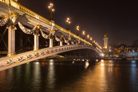Ornate bridge architecture illuminated after dark over the Seine in Paris, France, with warm lights reflected across the water.