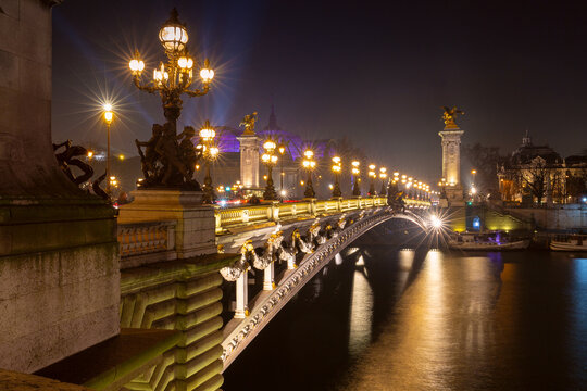 Ornate bridge architecture illuminated after dark over the Seine in Paris, France, with warm lights reflected across the water.