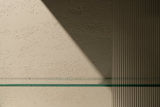 An empty transparent glass shelf against a travertine effect plaster wall with a fluted glass panel on the right and a diagonal shadow, providing a cosmetic product staging template with copy space.