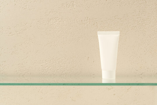 Blank White Cosmetic Tube on Glass Shelf Against Travertine Wall Background
