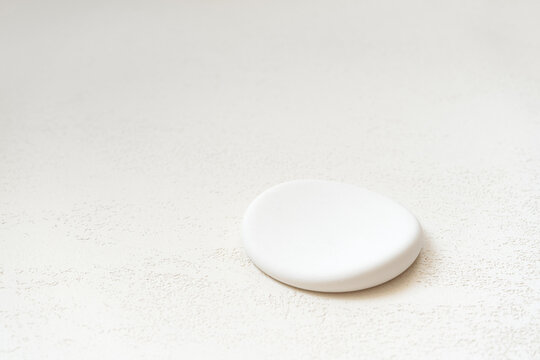 Single round flat white stone pedestal positioned in the lower right corner of a clean light neutral background, with generous copy space for cosmetic product placement and beauty advertising layouts.