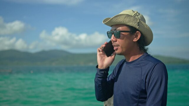 Man enjoying a phone conversation before ending the call on a sunny tropical beach, capturing communication, relaxation, vacation, travel, and a carefree seaside lifestyle.