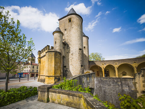 Historic Porte des Allemands in Metz, France, photographed on April 26, 2025. Medieval fortified city gate with round stone towers, defensive walls, bridge structures and arcades under a blue spring s