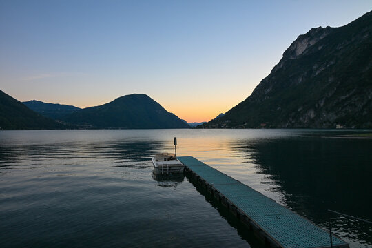Sunset over Lake Lugano with jetty and mountains in Porlezza, Italy