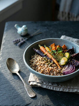 A grey ceramic bowl filled with cooked grains, roasted vegetables including carrots