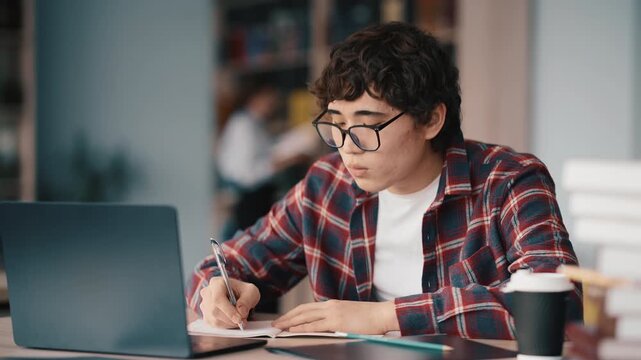 Student studying at desk with laptop and notebook wearing glasses