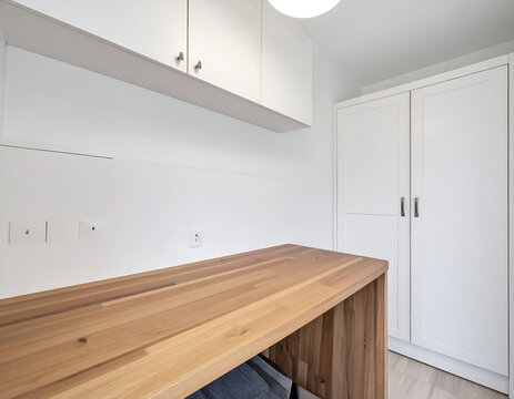 A modern home office nook featuring a wooden desk, white floating upper cabinets, and a white floor-to-ceiling wardrobe set against a clean white wall.