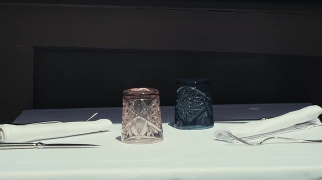 Elegant restaurant table set with crystal drinking glasses, folded napkins, and cutlery on a white tablecloth. Cozy fine dining interior prepared for guests before service. High quality 4k footage