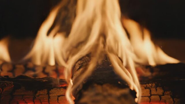 Flames dance and crackle over wood logs in a fireplace. The warm glow fills the room as smoke rises. People gather around to enjoy the warmth and light of the fire
