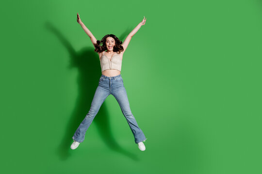 Happy young woman jumping in jeans against a vibrant green background expressing joy and energy in a studio shot