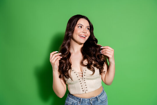 Smiling young woman with long wavy hair in casual crop top and jeans against green background, cheerful portrait expressing confidence and playful fashion