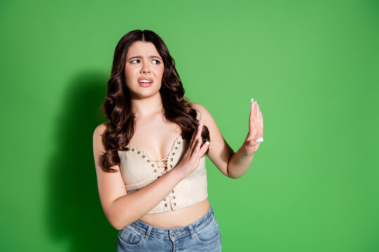 Young woman making a disgusted stop gesture against a green background expressing rejection, discomfort and refusal in a studio portrait