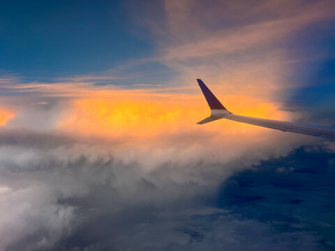 Commercial airliner wing floating above soft clouds at sunset