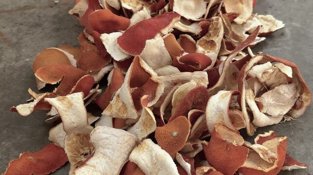Dried orange peels are piled on a gray concrete floor. Citrus zest, dried fruit, natural ingredient, organic waste