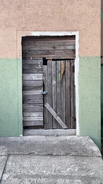 An old weathered wooden door with a padlock is set in a painted building wall. Rustic entrance, aged wood, vintage exterior, locked gate