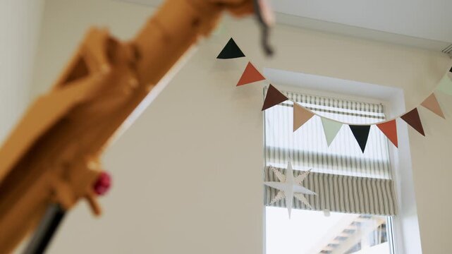 Bright children's room with a decorative bunting garland, window with blinds and a wooden toy in the foreground.