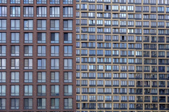 Two contrasting skyscraper facades dividing the frame vertically into brown and yellow brick patterns. Symmetrical window grid layout for minimalistic urban architecture backdrop.