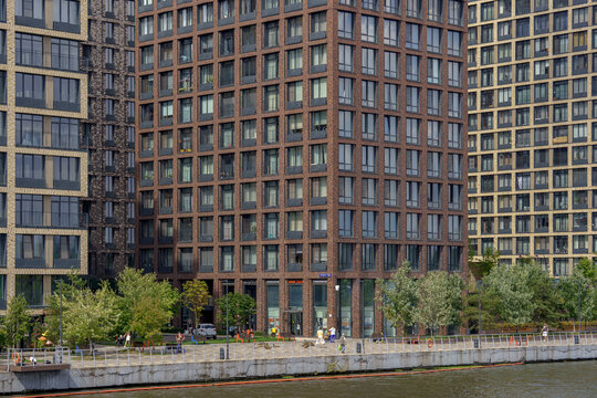 Modern residential skyscrapers on the river embankment as an urban landscape. Highrise apartment buildings with windows and green trees.