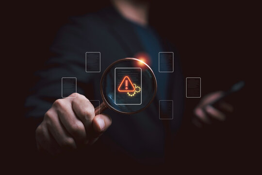 Businessman using magnifying glass to inspect data protection warning for cybersecurity, privacy, security risk, compliance, data breach prevention, digital audit and information protection.