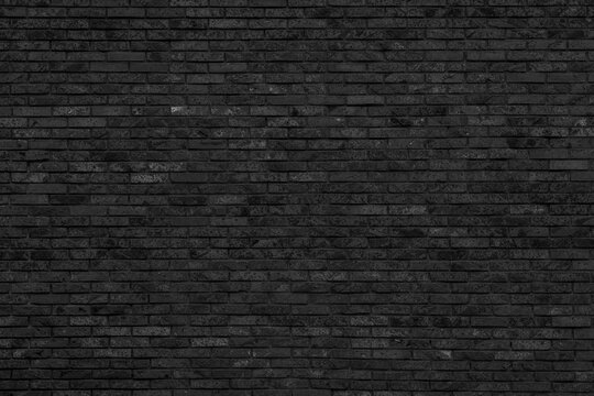 Black narrow clinker brick wall background with fine textured brickwork surface. Dark monochrome blocks layout for loft interior wallpaper.