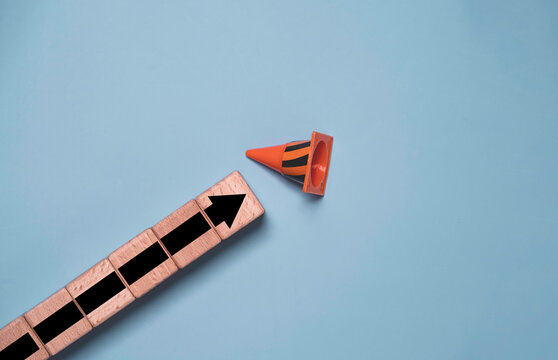 Wooden blocks with upward arrow approaching traffic cone for obstacle with challenge, business growth, progress, risk strategy, problem solving, overcoming barriers and path to success.