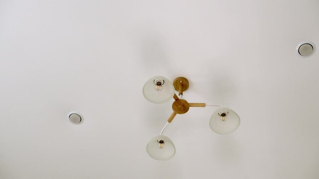Modern ceiling light fixture in a bright residential interior. Minimalist chandelier with three glass lamps on a white ceiling, viewed from below.