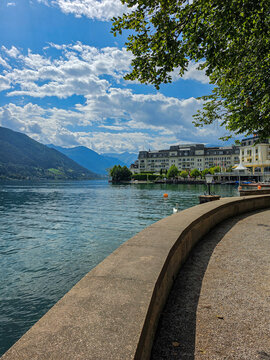 scenic lakeside promenade with alpine mountains and waterfront hotel under a dramatic summer sky, zell am see