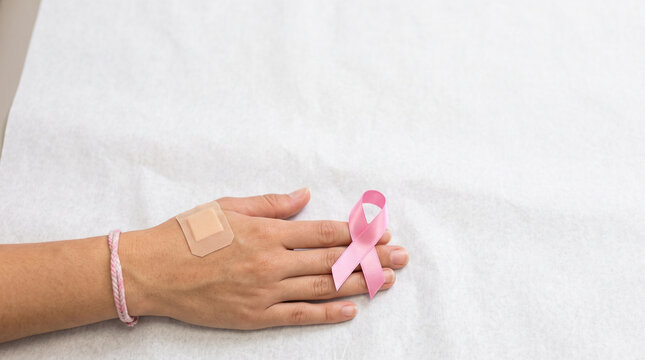 Hand with pink ribbon symbolizing breast cancer awareness and a band-aid on a white background