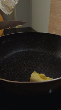 Butter Melts and Spreads Across a Black Cooking Pan in a Kitchen, Close Up View Shows a Basic Step of Food Preparation Slow motion Vertical video. Vertical video.