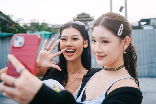 Two young women authentic Gen Z holding flower self style outfit selfie for social media shared experience moment in Asia local travel