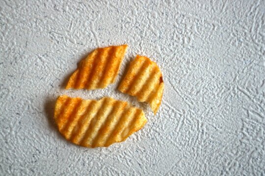 Ridged potato chips with reddish-orange savory seasoning, broken into three pieces.