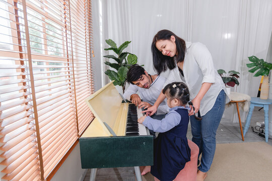 Happy family spending quality time together while learning to play the piano home are helping children practice music creating warm and supportive family environment.