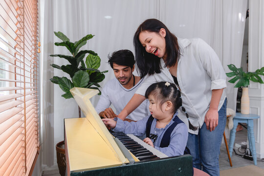 Happy family spending quality time together while learning to play the piano home are helping children practice music creating warm and supportive family environment.
