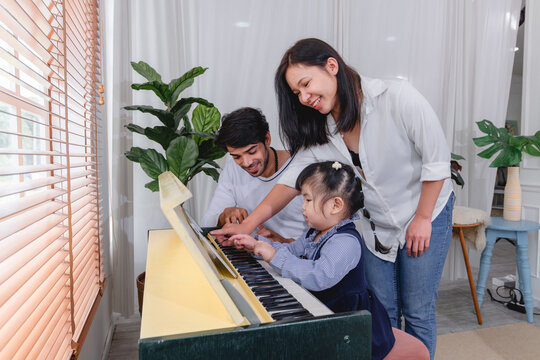 Happy family spending quality time together while learning to play the piano home are helping children practice music creating warm and supportive family environment.